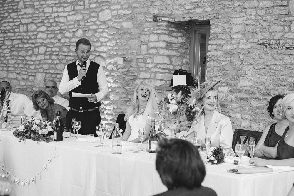Black and white photo, groom giving speech while bride laughs