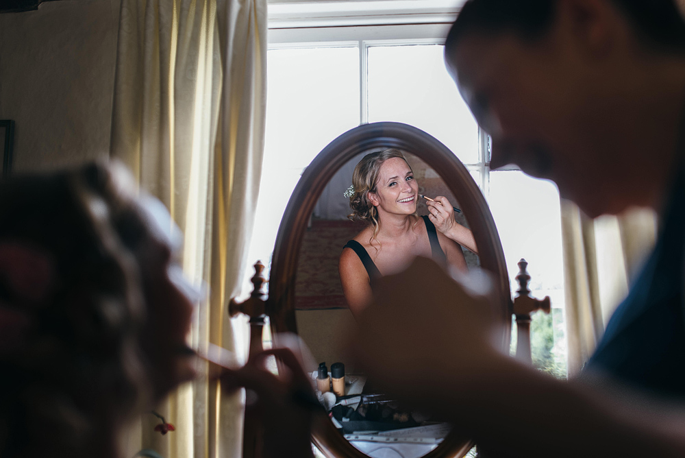 Bride smiling in mirror having makeup applied