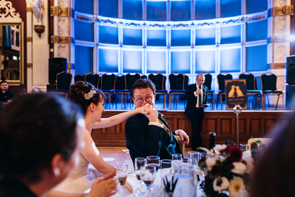 Groom kissing bride's hand at table