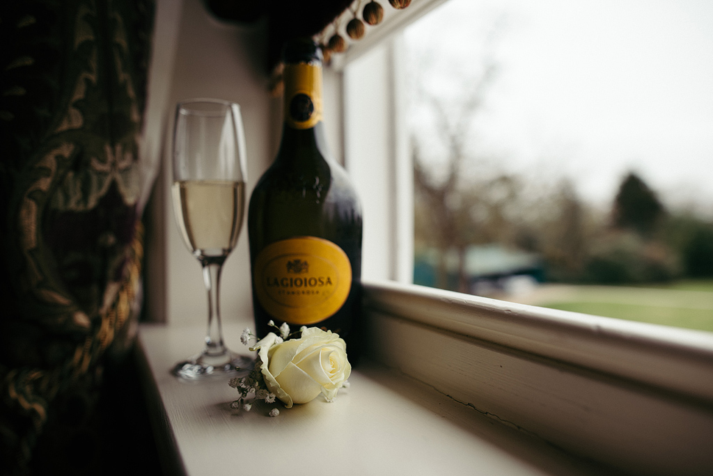 Bottle of champagne and glass, white rose, windowsill, wedding day
