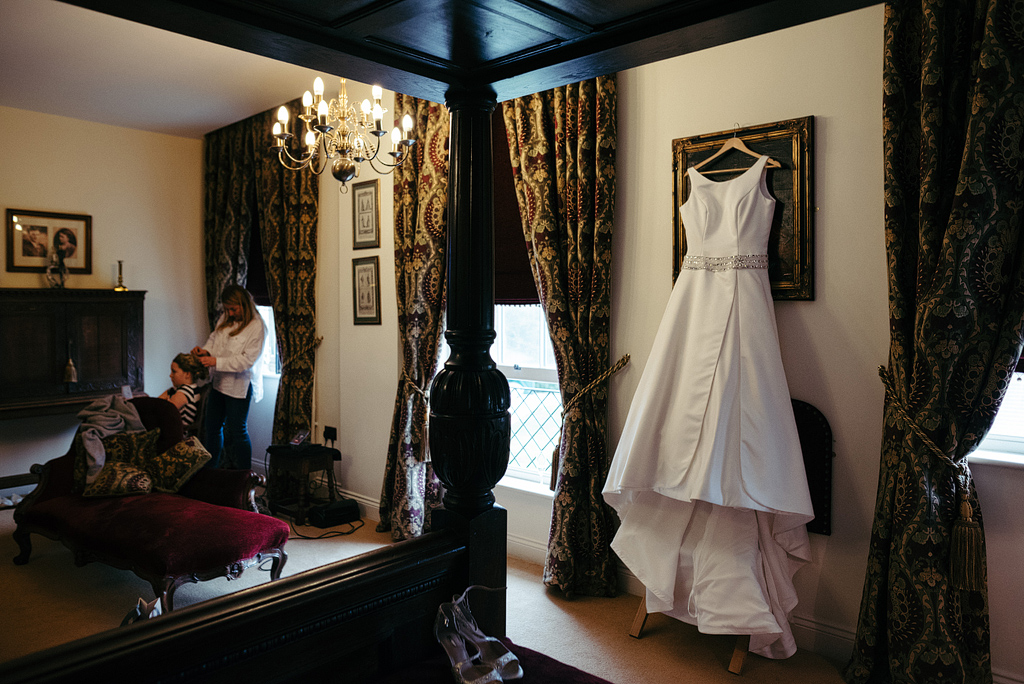 Bridal dress hanging in suite, stylist preparing bride's hair