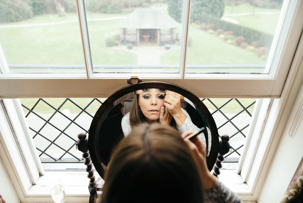 Bride applying makeup at vanity mirror.