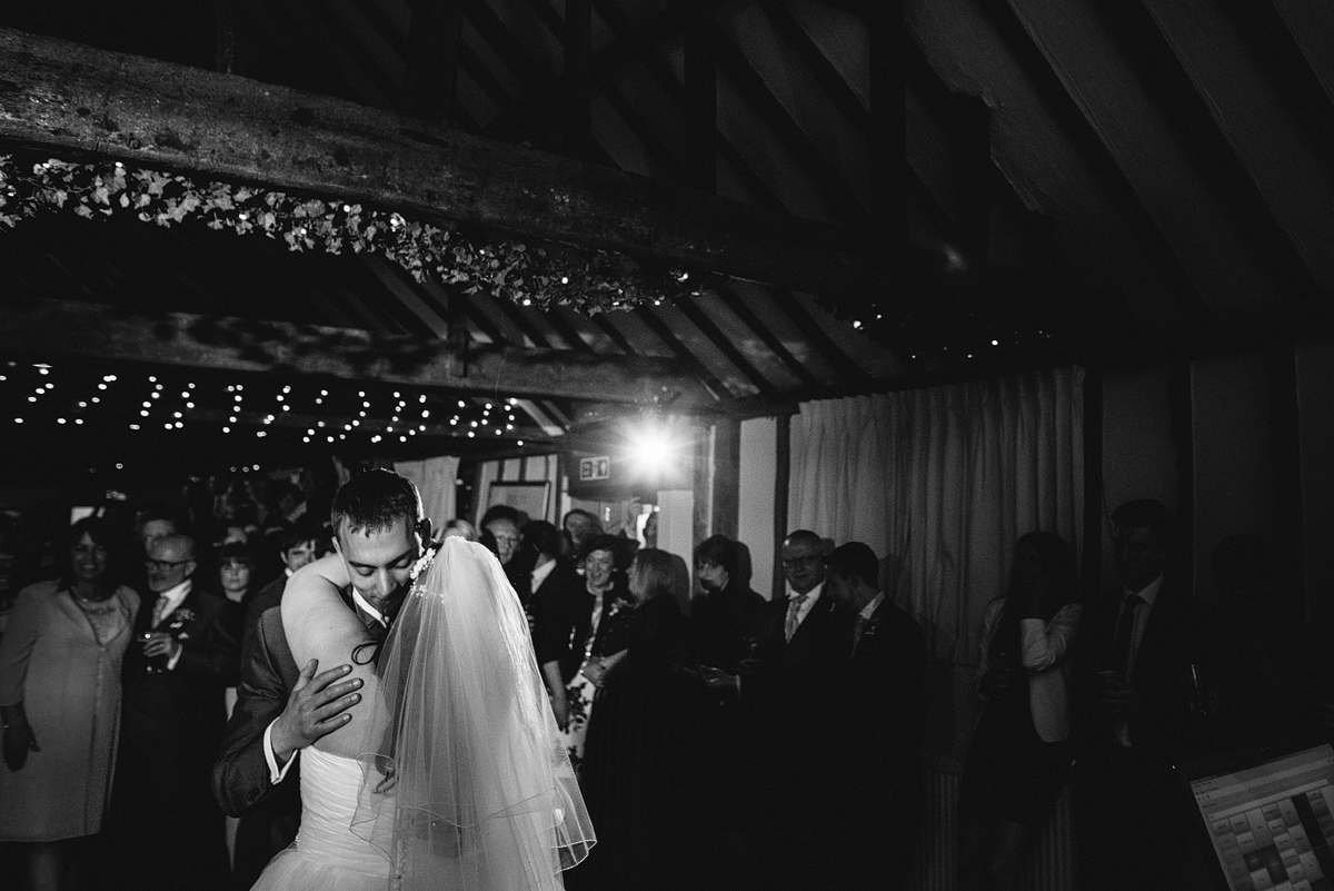 Black and white image of bride and groom dancing under lights in barn