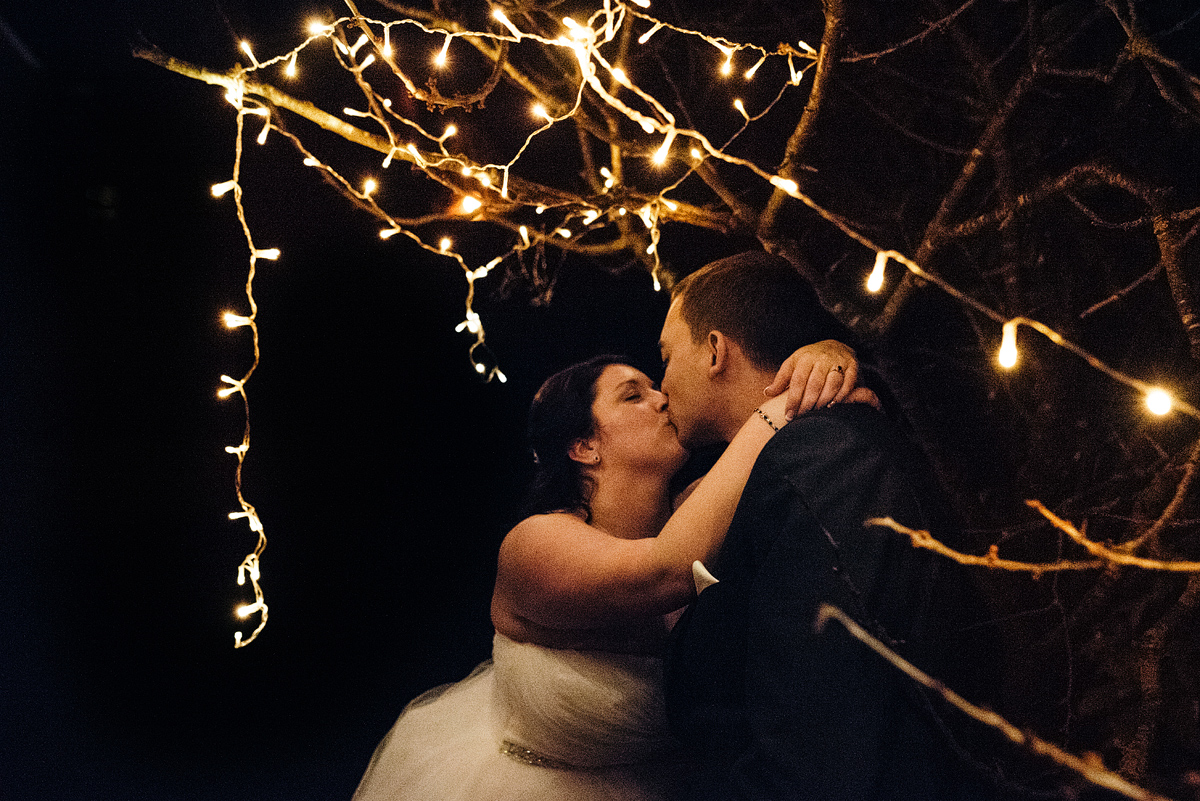 Bride and groom kissing outside at night under white lights