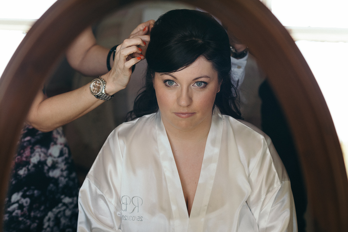Bride looking into vanity mirror as stylist pins her hair.
