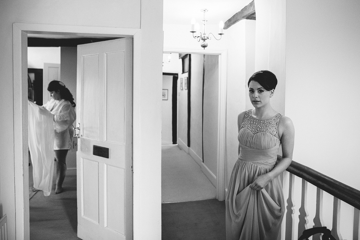 Bridesmaid waiting outside while bride behind half open door looks at dress