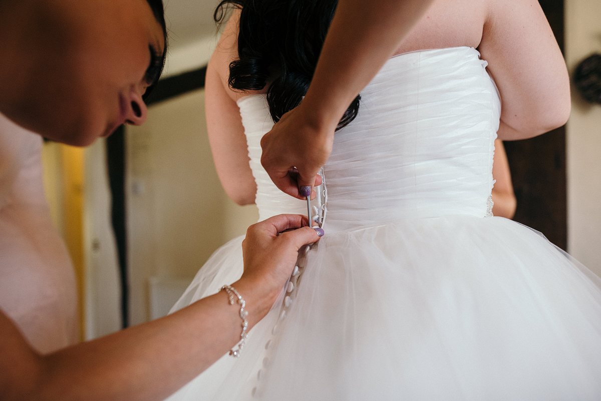 Woman threading bride's corset on dress.