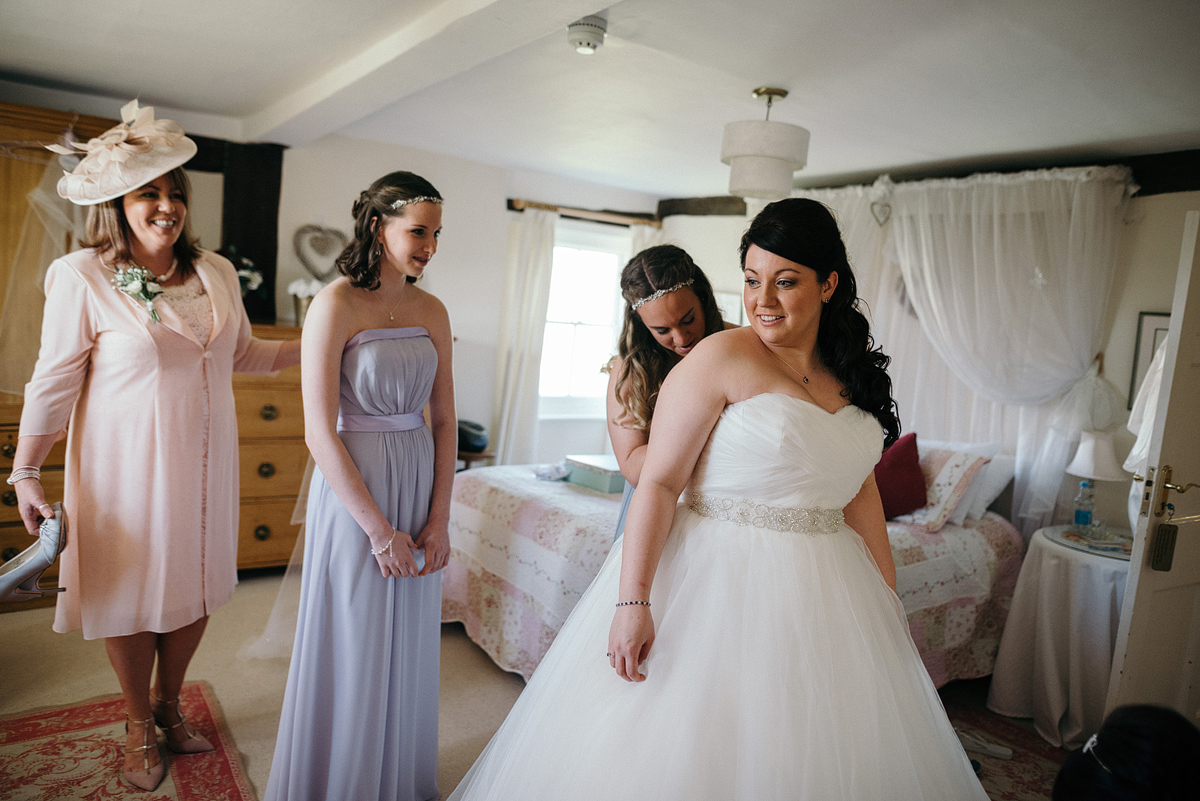 Bride being helped into dress as bridal party smiles.