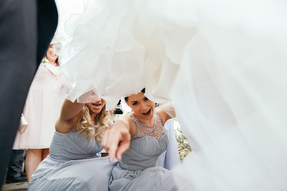 Bridesmaids smiling and laughing while looking under bride's dress.