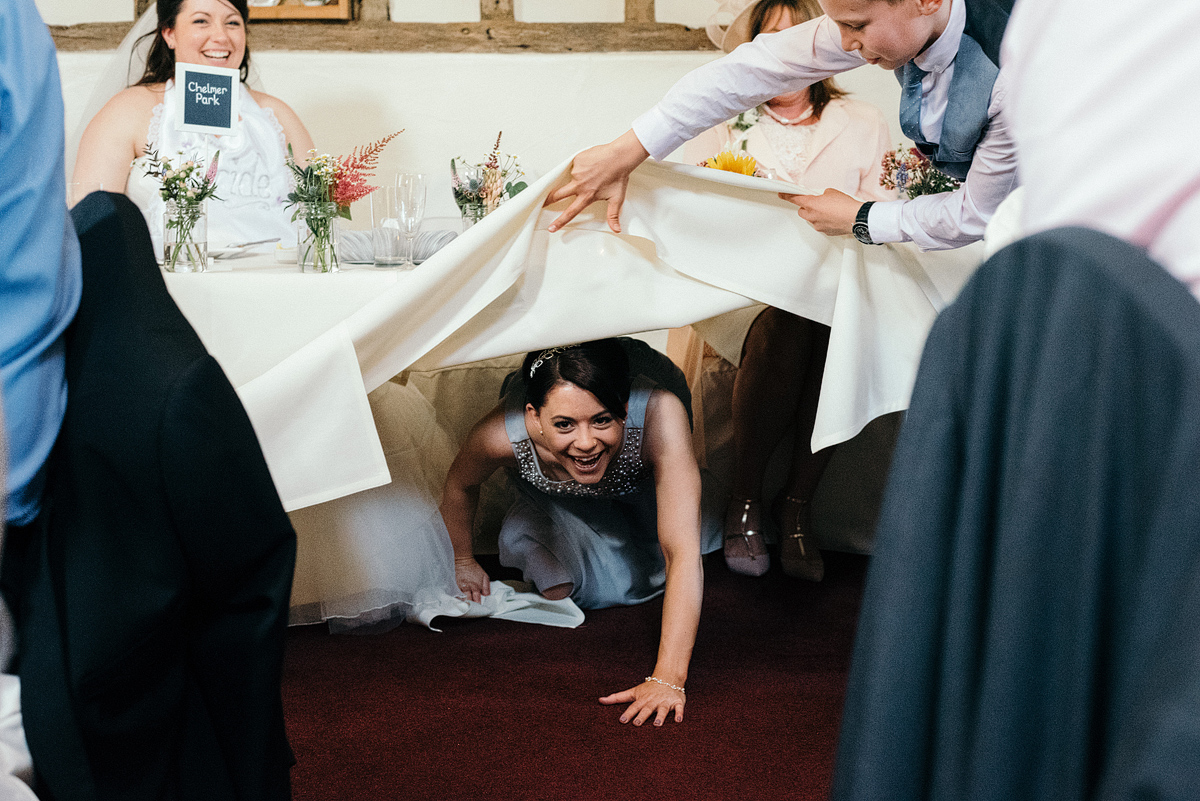 Bridesmaid laughing crawling under table.