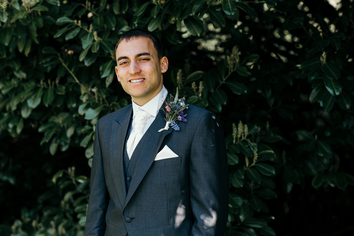 Groom smiling in shade under trees.